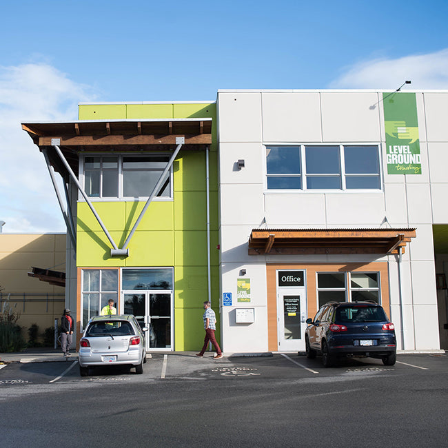 Exterior of Level Ground green, grey, wood trim building, man walking into cafè, blue sky