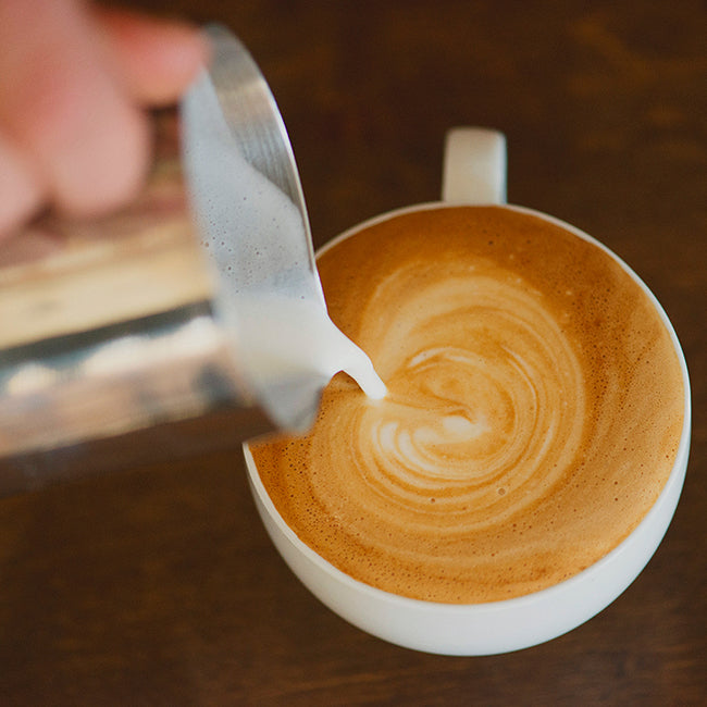 Steamed milk poured into latte mug on wooden counter